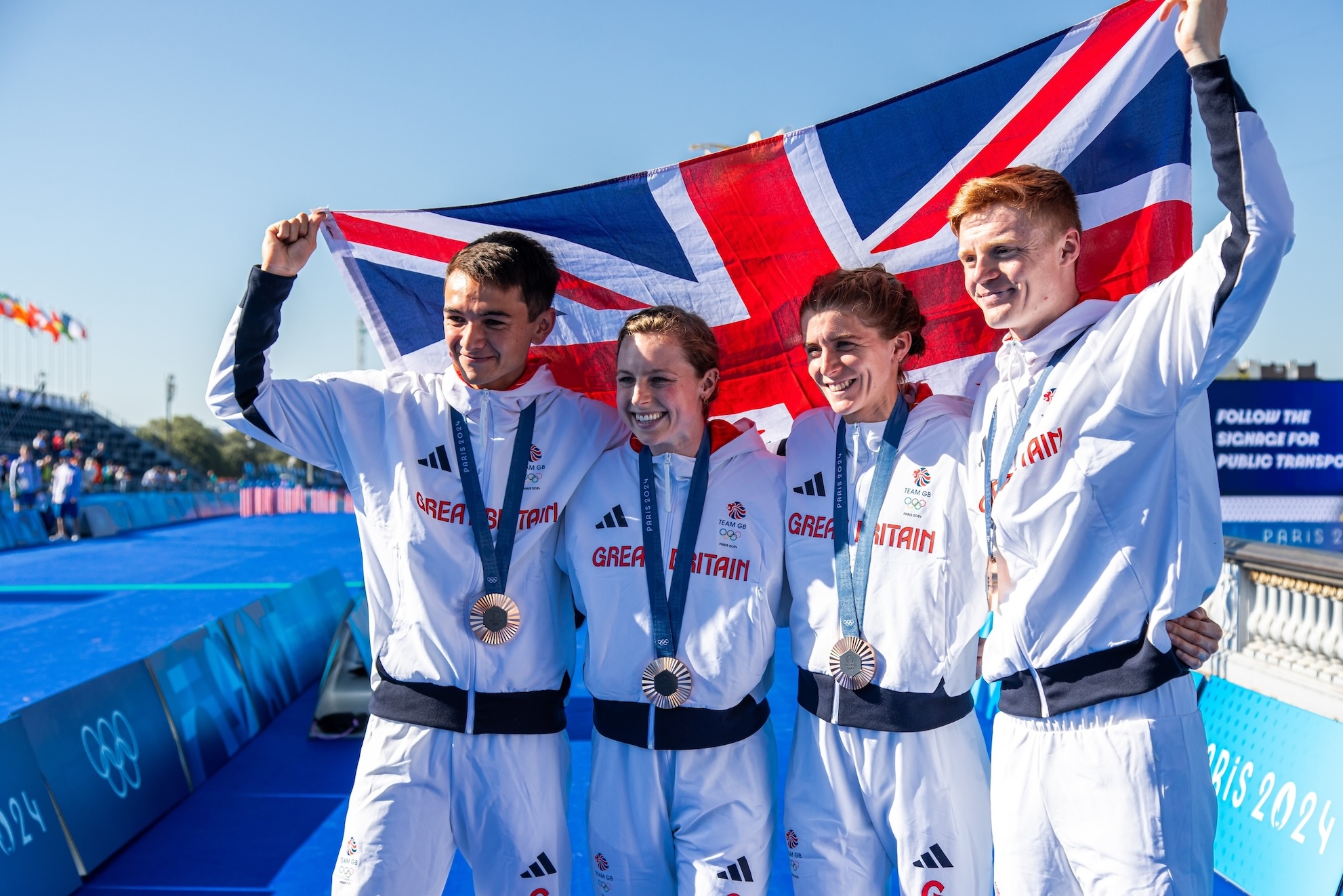 Team GB triathlon athletes celebrate with Union Jack at Paris 2024.