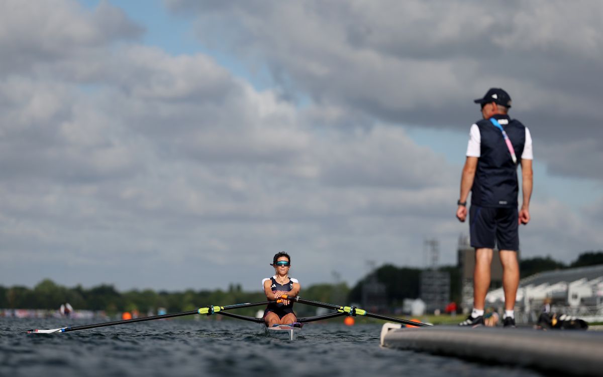 Imogen Grant rowing in the middle of the image, rowing away from camera. A coach stands on the dock to the right hand side.