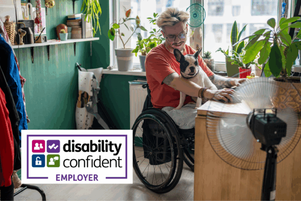 A young man in a wheelchair sits in a homeworking space with a dog on his lap