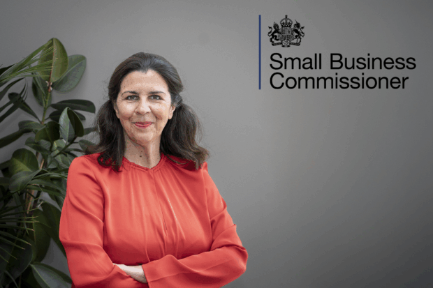 Emma Jones CBE, the Small Business Commissioner stands in front of a grey backdrop, next to a plant