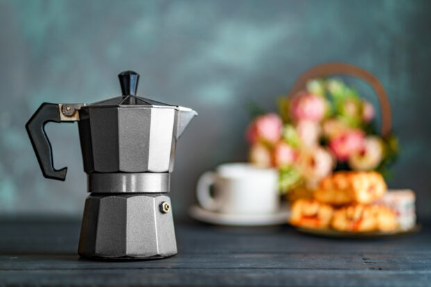 An image of a Moka pot in front of blurred flowers