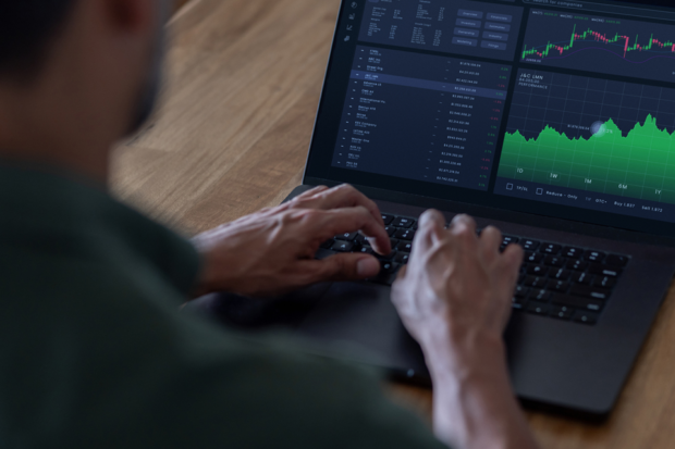 A man types on the keyboard of a laptop. The screen shows graphs and data.