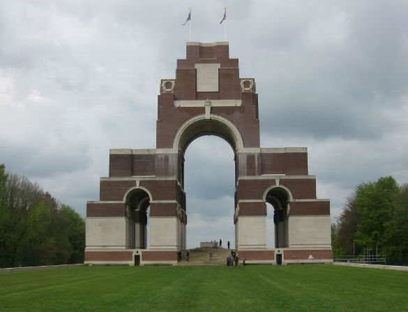 The Thiepval Memorial against a cloudy sky with a green lawn in front.