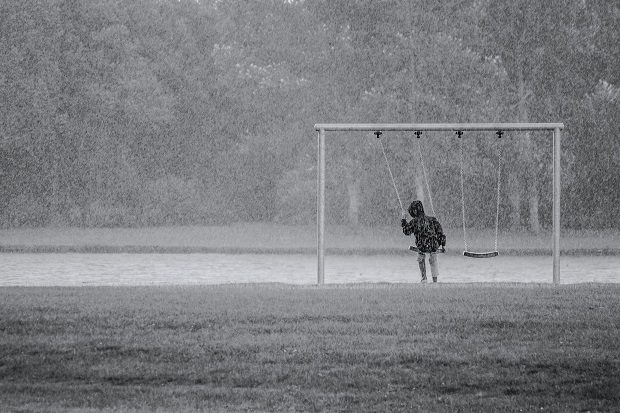 Boy in a park sitting on a swingset in the rain
