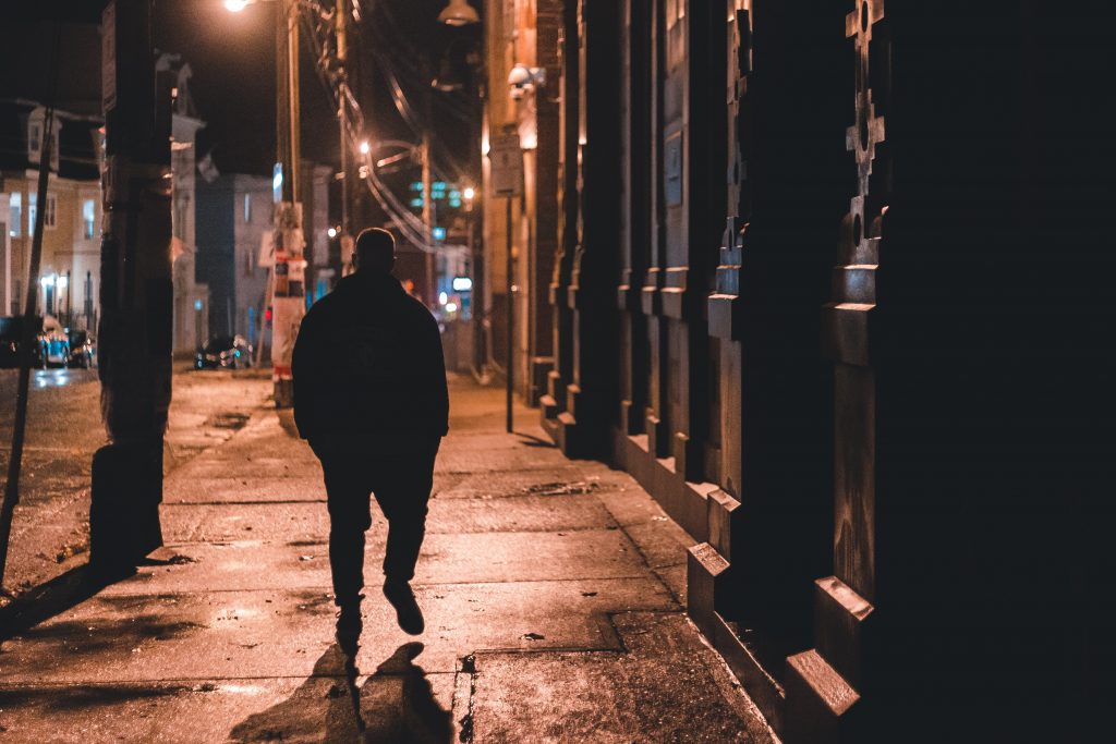 A man walking alone at night under street lamps in a city