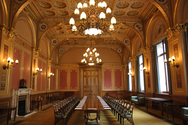 2 chandeliers and golden decorated ceiling. A dining table is set out throughout the length of the room