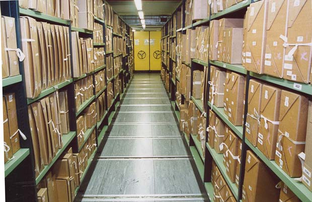 Boxed documents on shelves at The National Archives on one of the repository floors showing a corridor between two movable bays of shelving. The boxes are labelled with their document references.
