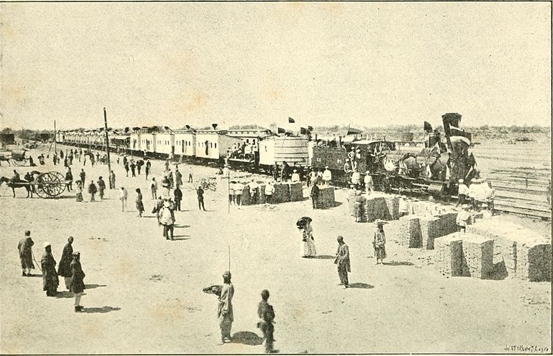 An old fashioned railway with a steam train stood still on the track, surrounded by locals and onlookers.