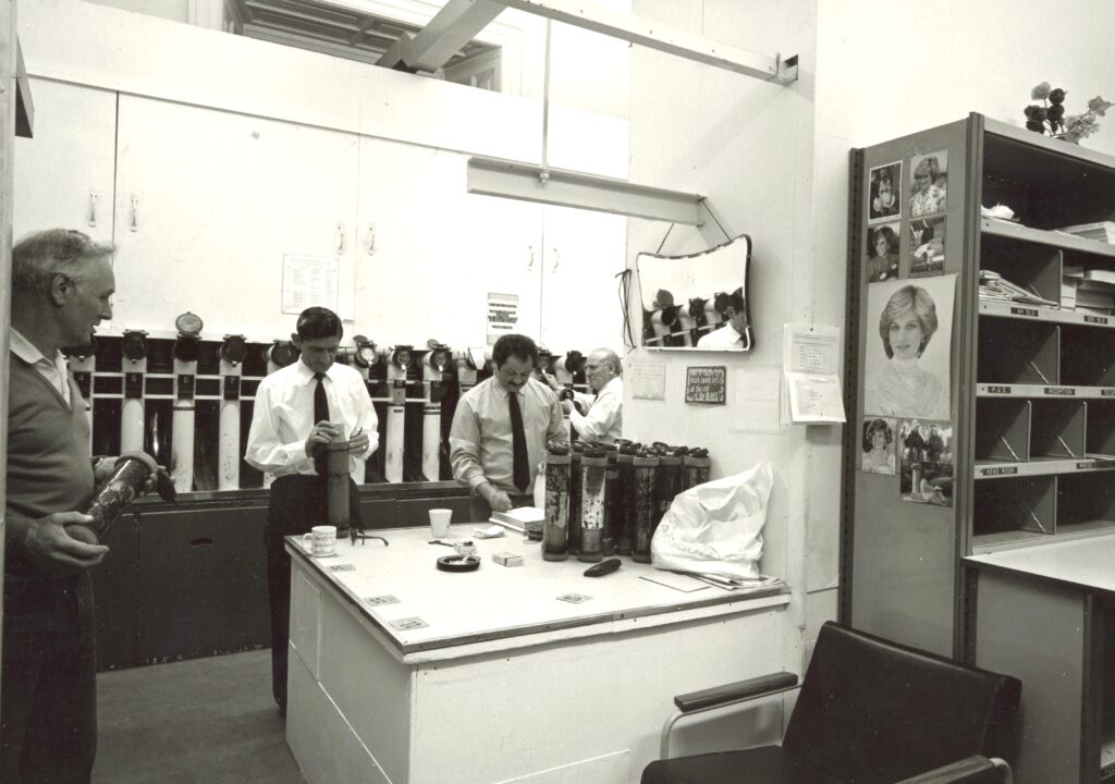 A room with a men in it, packing mail into tube to put it into one of the shoots on the wall