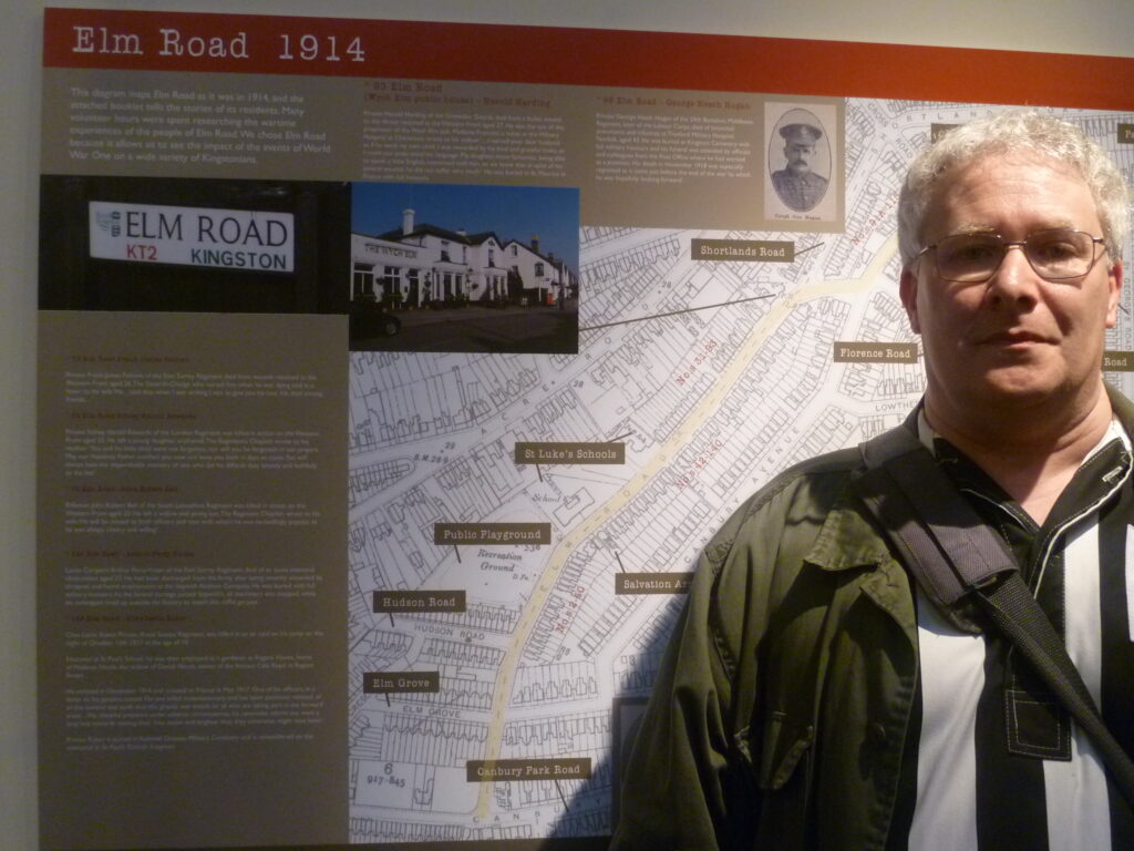 A photograph of one of Kingston Museum's volunteers, Dan Leissner, standing in front of a map of Elm Road containing information about the lives of its residents in 1914-1918.