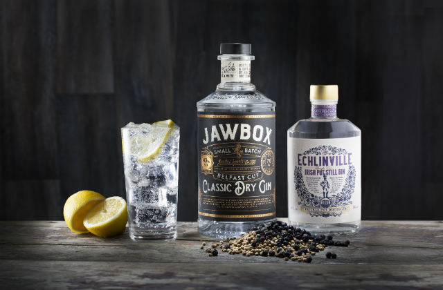An image of a glass of gin and tonic on a table next to two bottles of Gin labelled Jawbox and Echlinville.