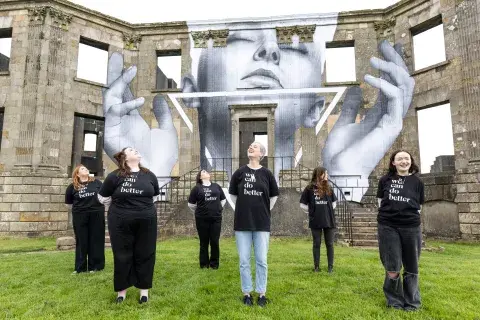 six young women standing in front of a historic building, featuring an image of a woman with open hands