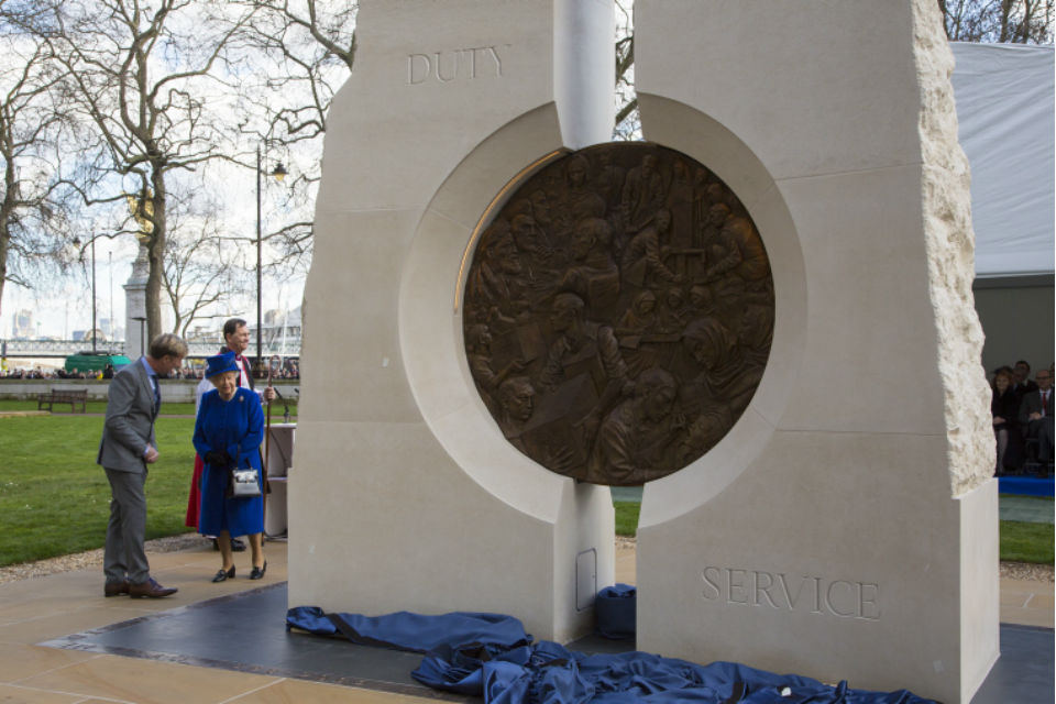 The Queen with man in suit and clergyman with memorial sculpture