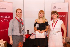 Two women and a man (left) at an exhibition stand with banners behind.