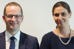 Bespectacled man in suit and tie and woman with necklace