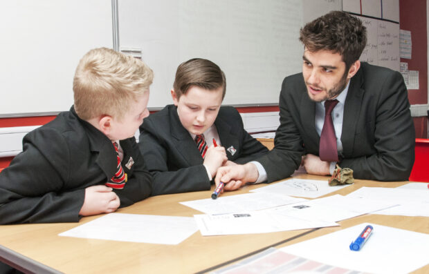 Teacher explaining a point to two pupils at secondary school.