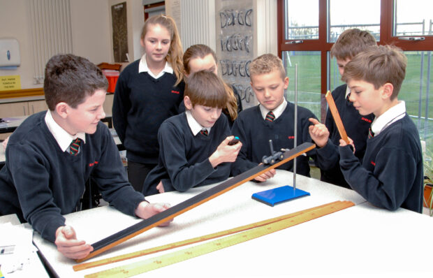 Pupils doing a physics experiment with a slope and wheeled toy.
