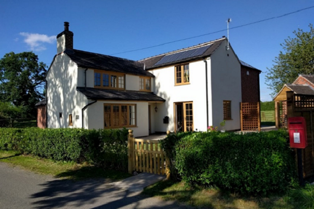 white cottage style house, with wooden window frames, a hedge to the front and wooden gate.
