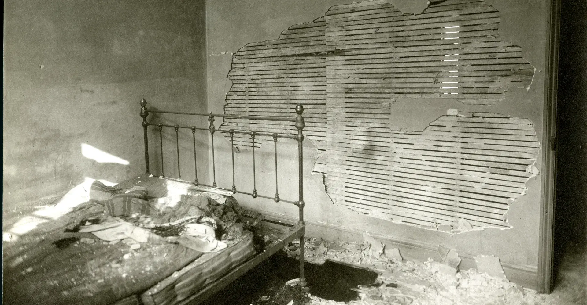 Bedroom with damaged wall and an iron frame bed