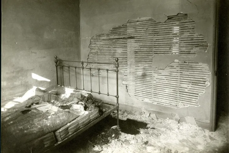 Bedroom with damaged wall and an iron frame bed