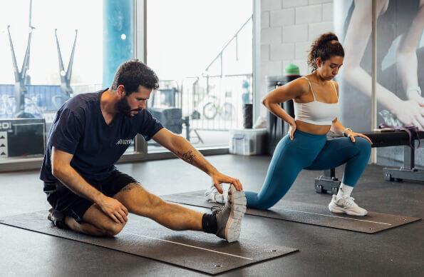 A man and woman stretch in a gym