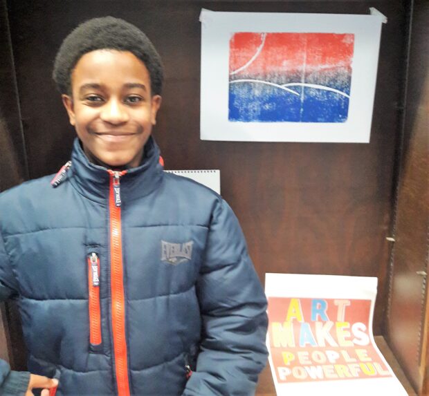 Photo of a smiling boy standing in front of artwork