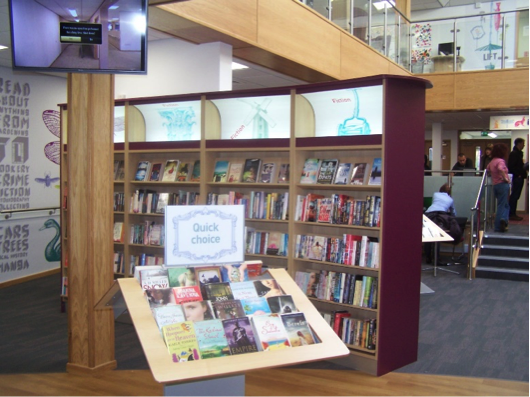 Photo of inside Stapleford library showing a TV screen and different book cases.