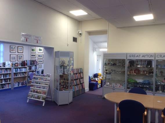 A photo of inside Great Ayton Discovery Centre, showing bookcases, a table and chairs and display cases