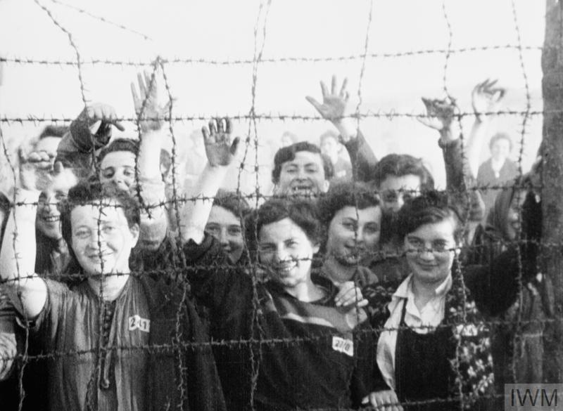Women waving from behind a barbed wire fence