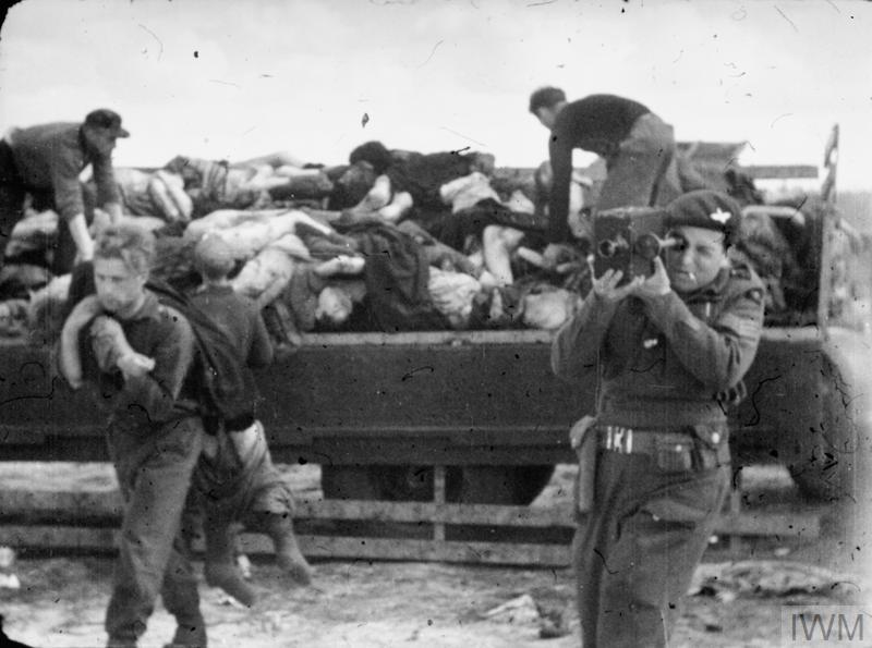 A British army cameraman during the liberation of Bergen-Belsen camp. Behind him, workers lift dead bodies from a flat bed truck and carry them for burial. 