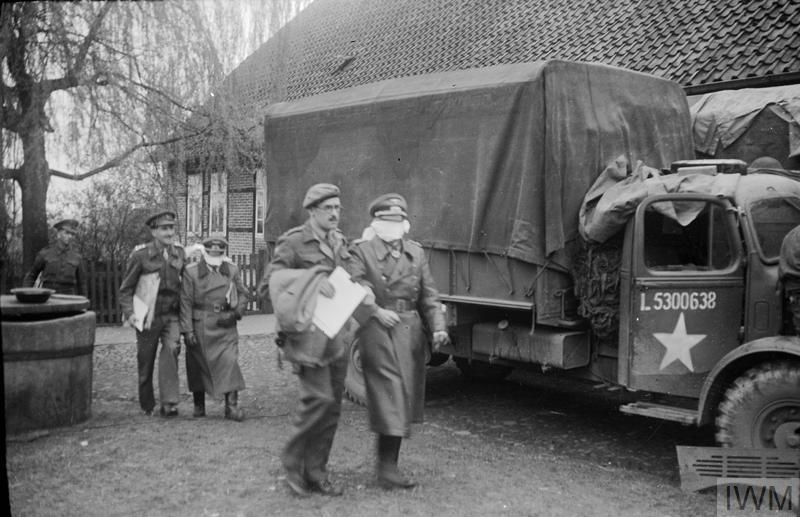 Two British officers escort two blindfolded German officers after negotiating a truce to manage the outbreak of infectious disease at Bergen-Belsen.