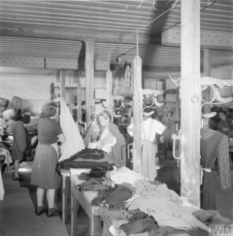 Former Bergen Belsen prisoners look over piles of  new clothing provided by relief workers, a female relief worker helps one woman choose a dress. 