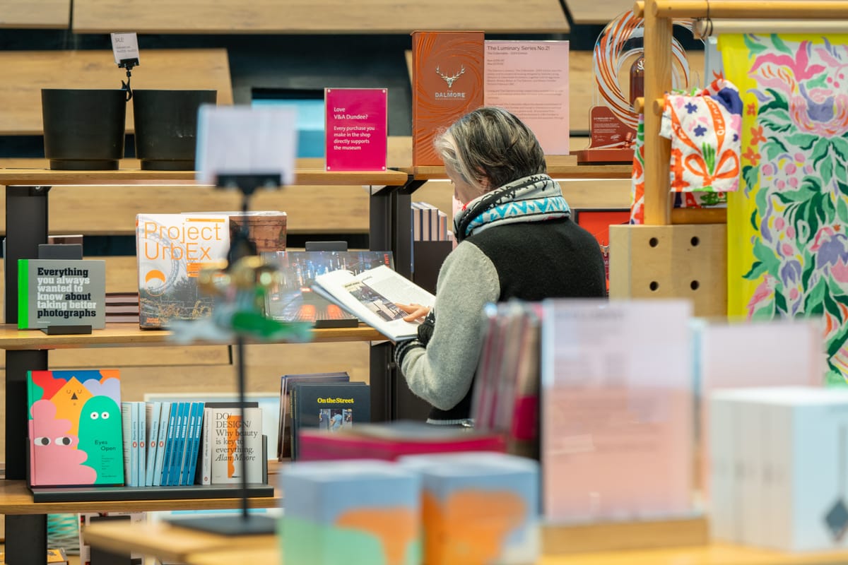 A person standing reading a book beside a bookcase.