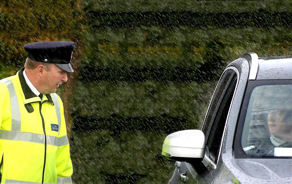 An MGS guard stands in the rain, talking to a visitor through a car window. 