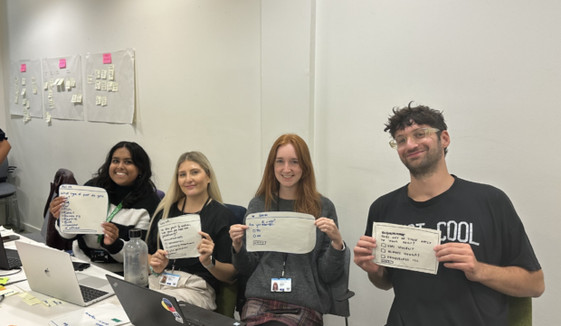 4 members of the user-centred design community holding up their paper prototype sketches.