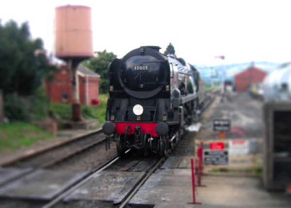 Black steam train approaching a foot crossing.