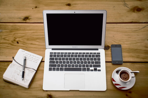 A desk with a laptop showing a blank screen, a notepad, a cup of coffee and a mobile phone