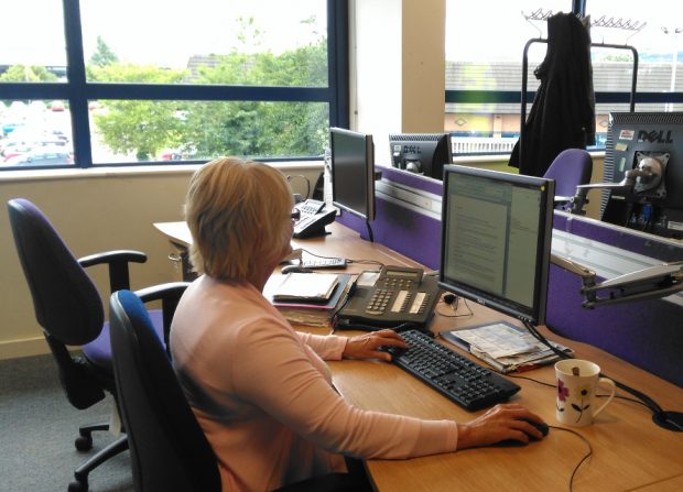 A webchat adviser sits at their desk looking at a computer monitor, reading from a word document. The text on the monitor is blurred and not legible.