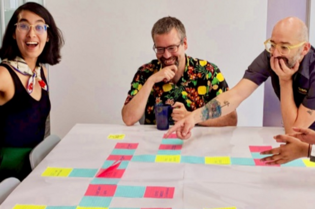 Three members of the Canadian Digital Service, laughing and smiling, around a table on which there is a large assortment of post it notes.
