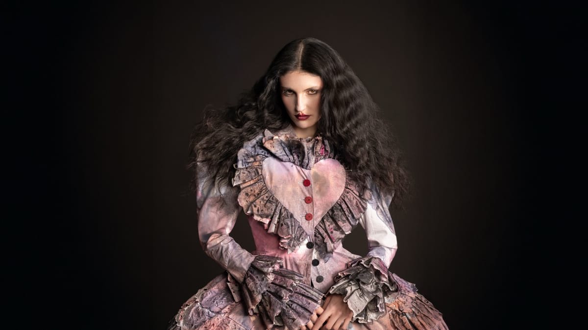 A model wearing a pink dress with a love heart detail against a black background.