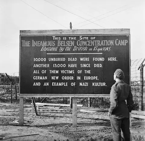 A soldier stands in front of a sign erected by British Forces at the entrance to Bergen-Belsen concentration camp, Germany, 29 May 1945. 