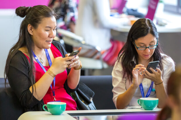Women in Digital event attendees Jenny Murray and Zoe Gould on mobile phones interacting with Slido questions during the event