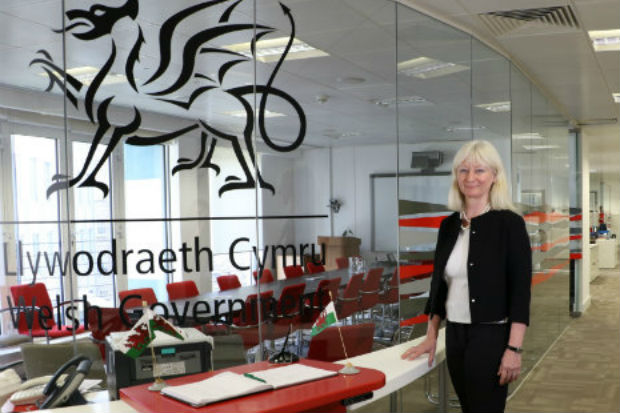 Shan Morgan, Permanent Secretary of the Welsh Government, standing by a glass fronted office with the Welsh dragon imprinted on in it.