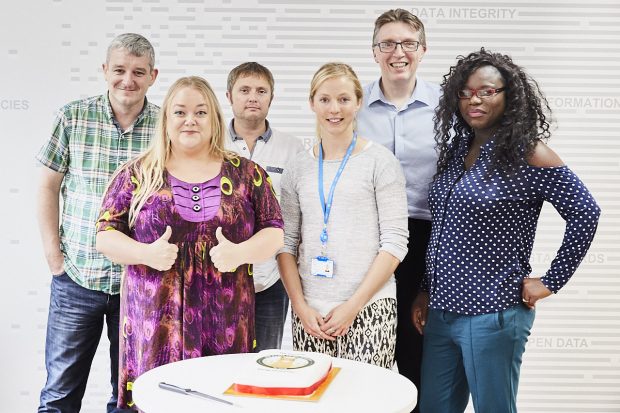 6 members of the team standing behind the llama cake.