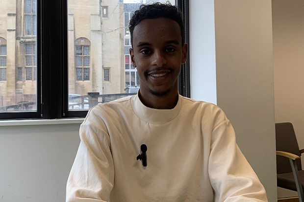 A man wearing a white jumper, smiling at a camera.