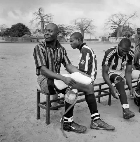 An amputee with a prosthetic limb sits on a bench in football uniform.
