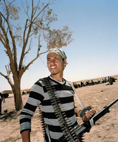 The anti-Gaddafi uprising and Civil War in Libya (2011). A man holds gun and has a belt of bullets wrapped over his shoulder while looking into the distance. 