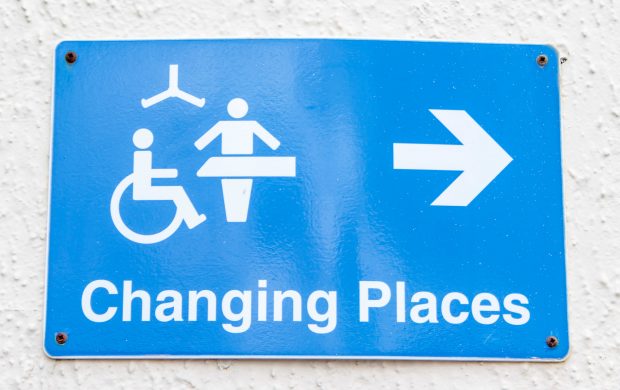 The Changing Places logo is in white against a bright blue background. The logo shows a wheelchair user, a hoist, and an adult changing bench and an arrow pointing to the location of the changing place.