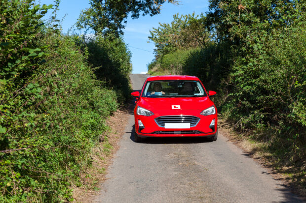 Red car with L plates driving down narrow country lane