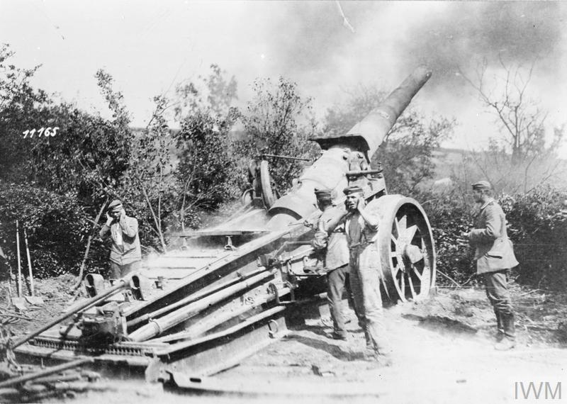 Four German troops stand next to a German 17cm heavy artillery gun firing. 
